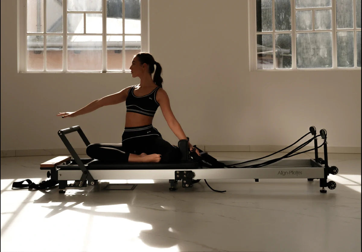 Žena u Être Noir et Blanc tajicama i topu na pilates reformeru u stretching vježbi