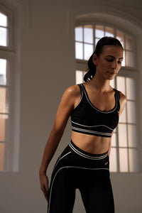 Crni sportski set Noir et Blanc Être - tajice i top s bijelim prugama i logom, artistička indoor fotografija, premium ženska sportska odjeća